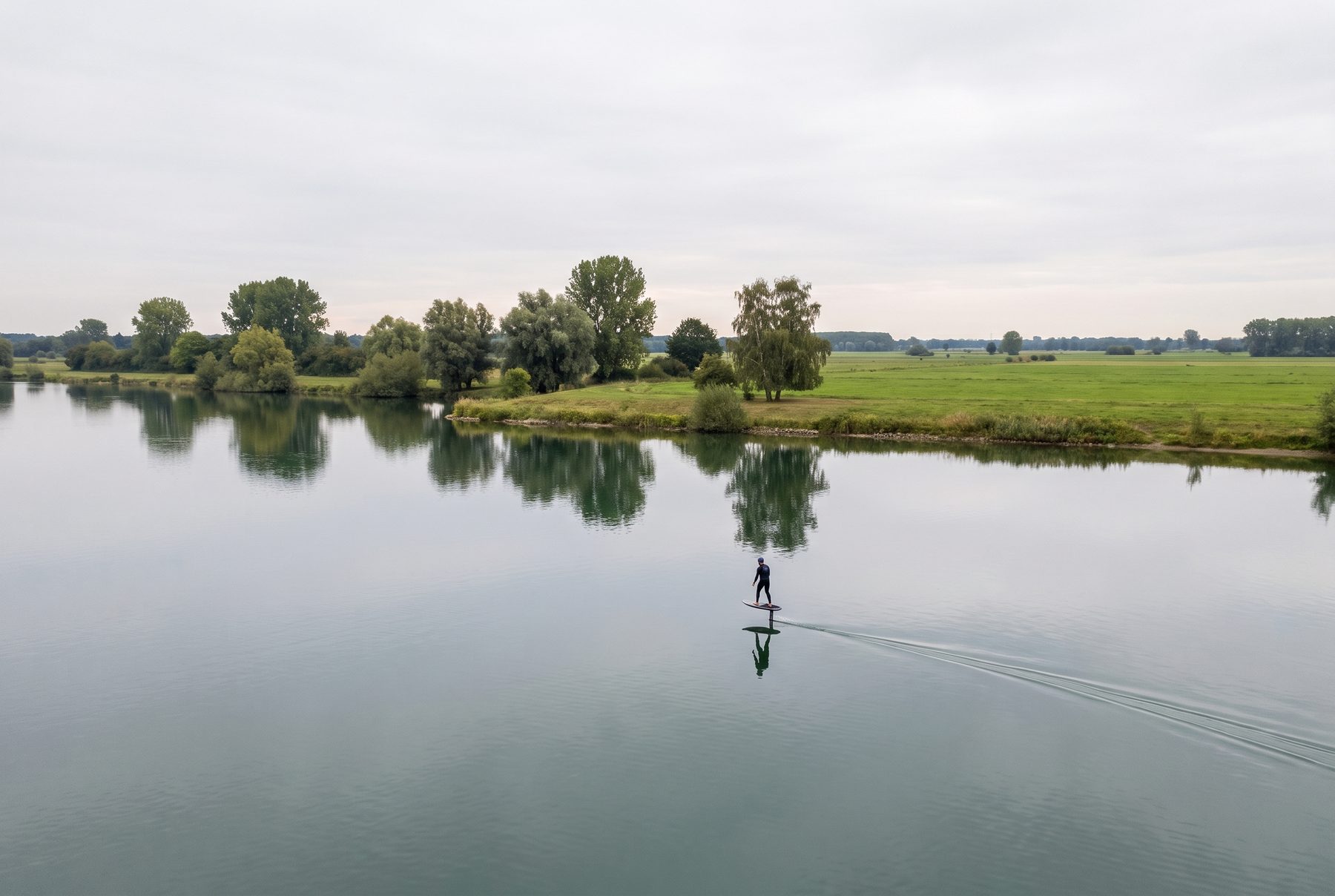 Foiler auf dem spiegelglatten Fühlinger See, flaches Ufer mit Bäumen